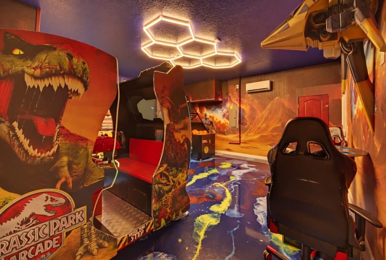 Themed arcade room with racing cabinets, hex ceiling lighting, and a painted wraparound mural at an Orlando vacation rental
