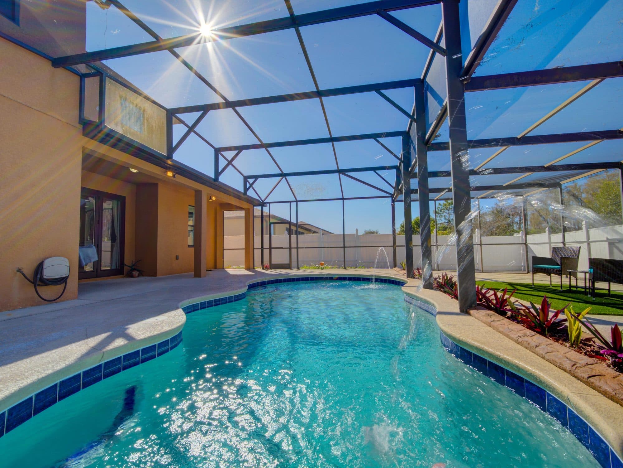 Sunlit screened pool with waterfall jets and tropical planting at a Central Florida vacation rental home