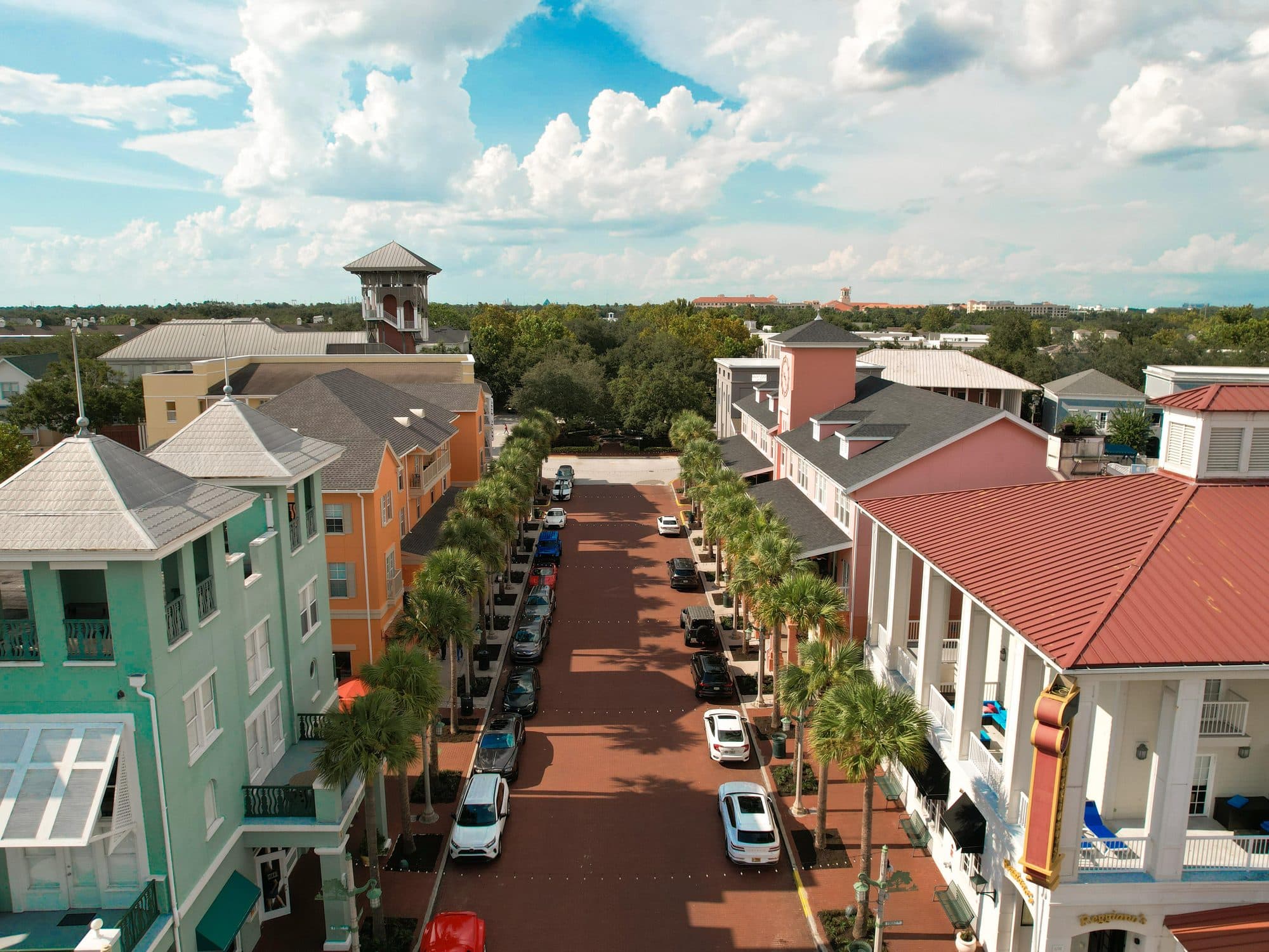Drone aerial of a Celebration Florida town centre street lined with palms and pastel buildings near Orlando vacation rentals